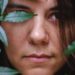 Fernanda Saad em um close-up, parcialmente escondida por folhas, simbolizando introspecção, força e determinação na experiência de morar fora.