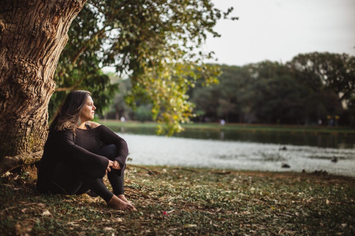 Fernanda Saad sentada ao ar livre à beira de um lago, refletindo, simbolizando a transição de estar presa na mente para se conectar com a vida.
